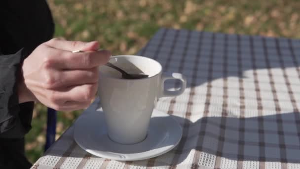 外のテーブルでドリンクカップを閉じると 女性は秋に通りのカフェでティースプーンでお茶に砂糖を干渉します — ストック動画