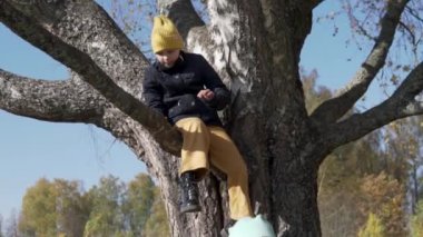 Yavaş çekimde, kız sonbaharda parkta bir ağaçtan iniyor.