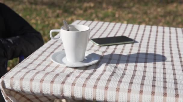 Kain meja di atas meja dengan bubur teh dan ponsel berkembang dari angin di luar pada musim gugur — Stok Video