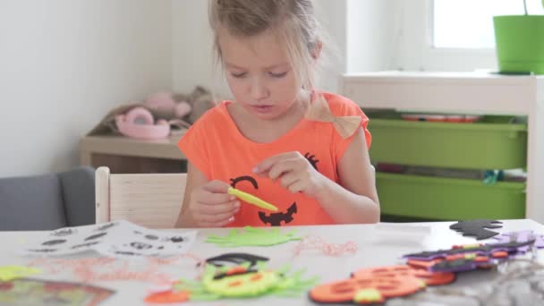 A little girl makes crafts for the Holiday Halloween at home from colored paper — Stock Video