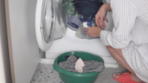 Een vrouw haalt de was uit de wasmachine en legt hem in het wasbekken. — Stockvideo