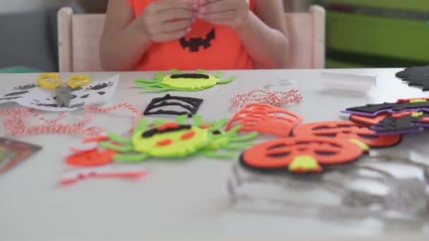 Gros plan, une petite fille fait des décors pour Halloween à partir de papier coloré à la maison à la table — Video