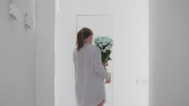 Yüzünde nemlendirici maske olan bir kadın sabahları banyoya beyaz kasımpatı vazosu taşır.