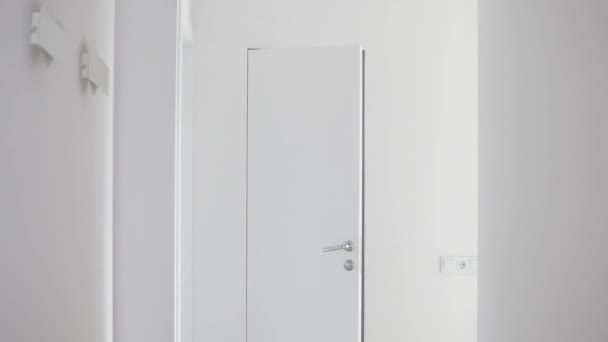 En kvinna i skjorta och en mask i ansiktet kommer ut ur badrummet med en vas av vita krysantemum — Stockvideo