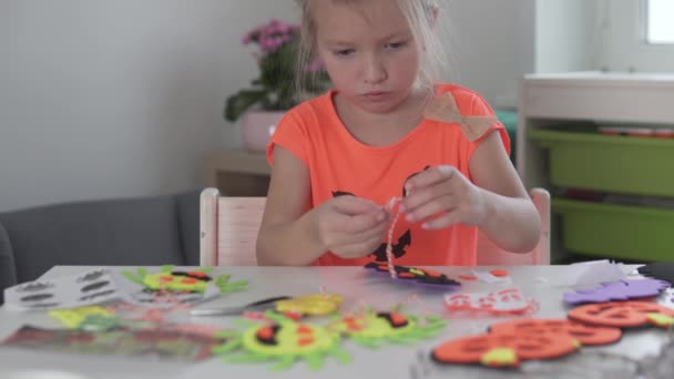Une petite fille apprend à nouer un nœud sur les cordes pour accrocher des décorations pour la maison à Helloween — Video