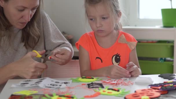 Die Lehrerin und das Mädchen basteln aus farbigem Papier eine Verzierung für das Feiertags-Halloween — Stockvideo