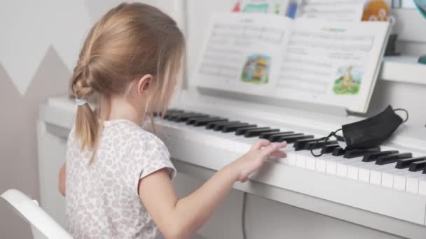 Petite fille jouant du piano électronique sur les notes pour enfants à la maison, la vue de dos — Video