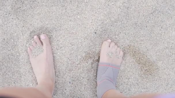 Close-up van een vrouw is benen van een atleet op het zand in een enkelband — Stockvideo