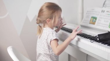 Sevimli küçük bir kız evde elektron piyanosu çalıyor.