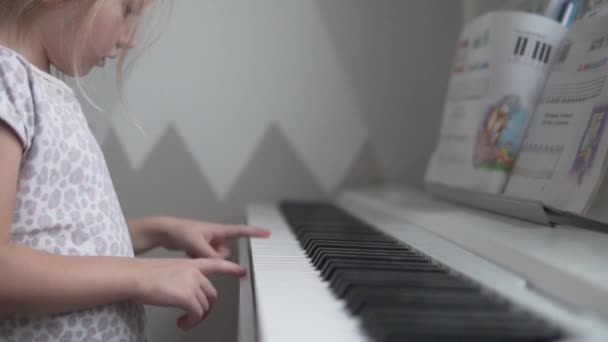 Uma menina aprende a tocar as notas do piano em casa — Vídeo de Stock