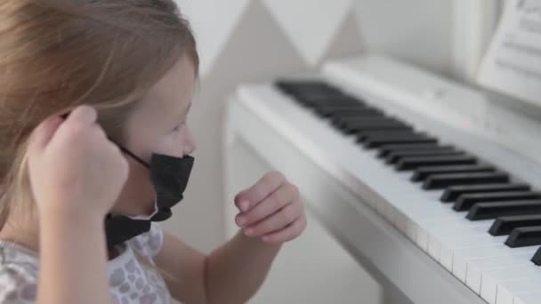 Uma menina usa uma máscara médica no rosto e toca piano — Vídeo de Stock