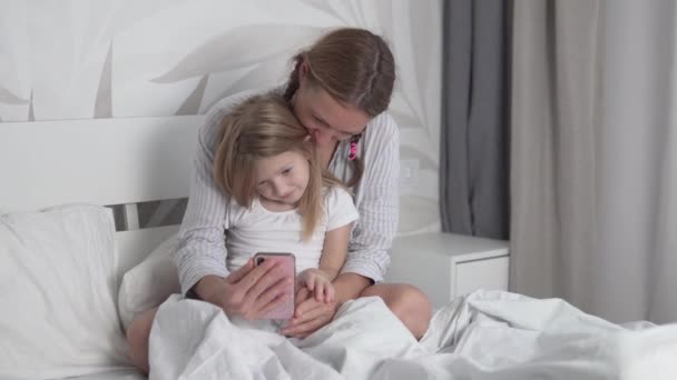 Μια μητέρα και μια μικρή κόρη επικοινωνούν από το τηλέφωνο μέσω video link με τον σύζυγό της το πρωί από το κρεβάτι — Αρχείο Βίντεο