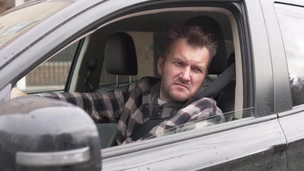 Um homem feliz está sentado em um carro e acena sua mão na janela aberta — Vídeo de Stock