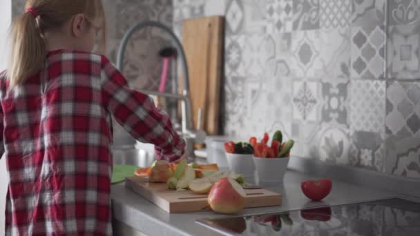 Una bambina carina e sua madre hanno messo la frutta a fette su un piatto in cucina — Video Stock