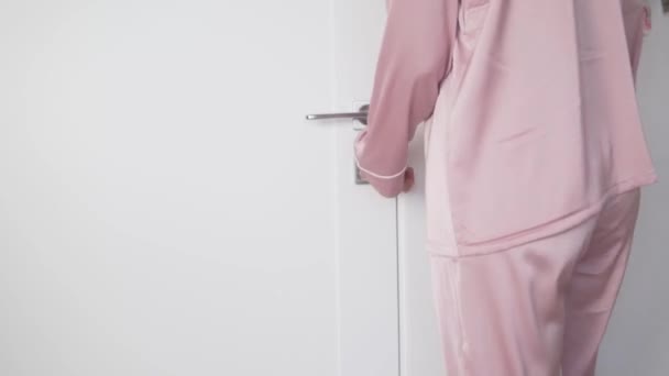 Primer plano, una mujer en pijama rosa abre la puerta y sale de la habitación — Vídeos de Stock