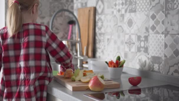 Une petite fille dépose des fruits tranchés, des poires, des pommes et des kaki dans une assiette à la maison dans la cuisine — Video