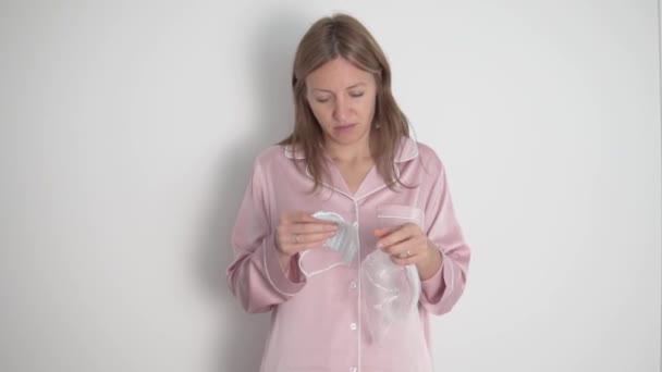 Uma mulher de lindo pijama rosa coloca uma máscara médica em seu rosto e começa a dançar contra um fundo branco — Vídeo de Stock