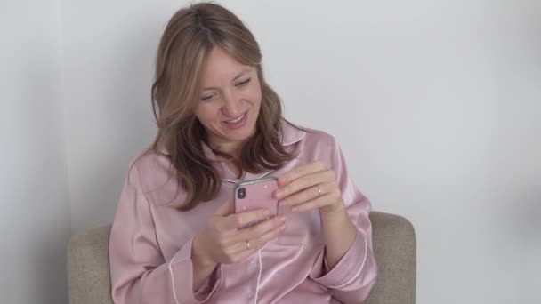 Een mooie vrouw zit in een stoel met een mobiele telefoon en leest het nieuws op het internet — Stockvideo