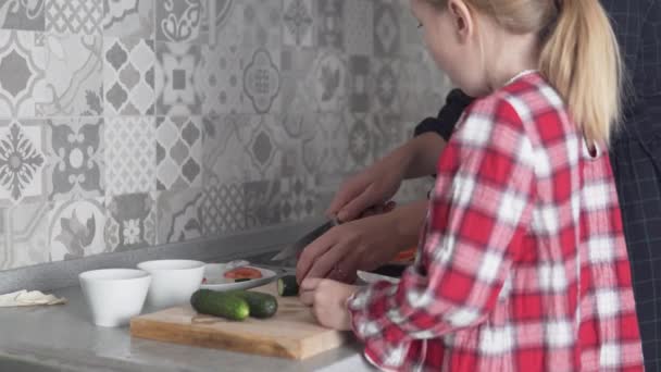 Una niña y su madre cortan pepinos en la cocina de la casa — Vídeos de Stock