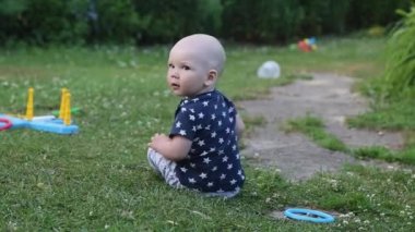 Küçük kel bir çocuk yazın çimlerde sürünür.