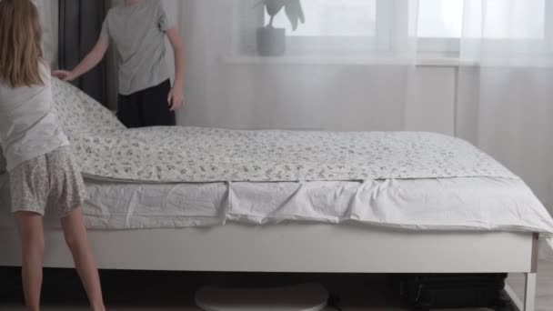 Crianças, um menino e uma menina, limpam a cama de seus pais pela manhã — Vídeo de Stock