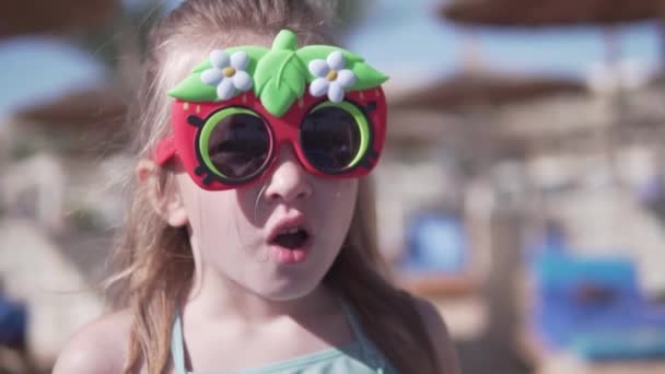 Een vrolijk meisje met een zonnebril op het strand in de zomer — Stockvideo