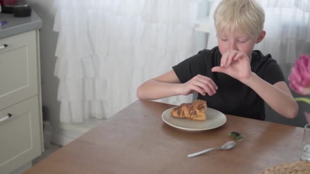 The boy removes the orthodontic plate from his teeth and eats a chocolate croissant at home — Stock Video