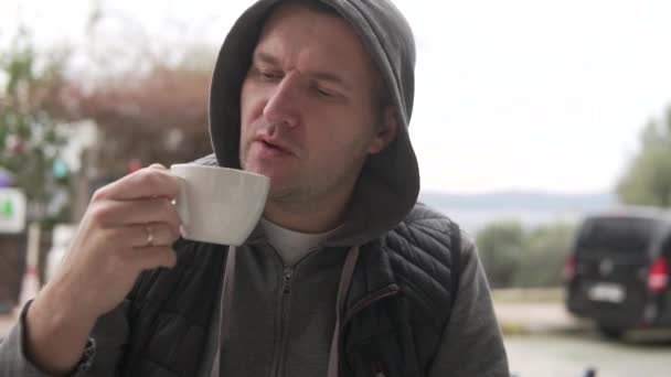 Ein brutaler Mann trinkt Kaffee an einem Tisch in einem Café auf der Straße, Nahaufnahme — Stockvideo