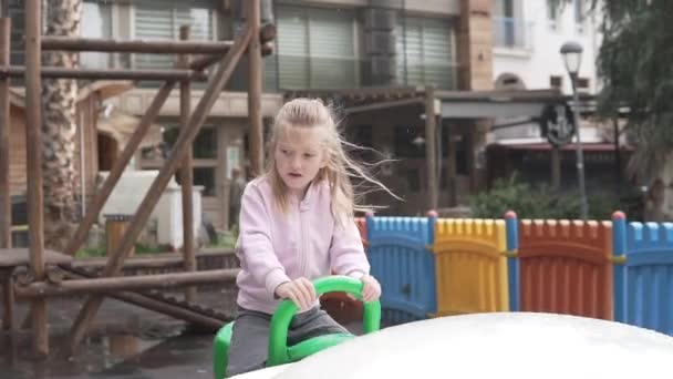 En söt liten flicka rider en sväng i parken på våren i regnet — Stockvideo