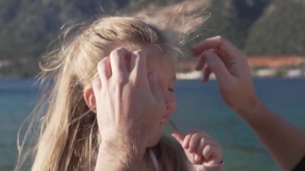 Close-up, slow-motion schieten, een mensenhand verwijdert haar van het gezicht van een klein meisje tegen de achtergrond van de zee — Stockvideo