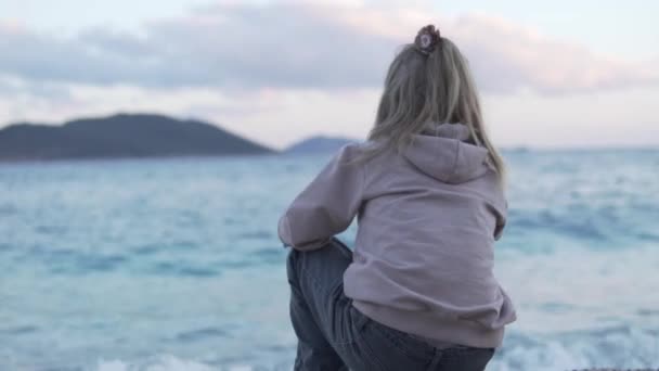En vacker liten flicka tittar på havet på stranden på kvällen, — Stockvideo