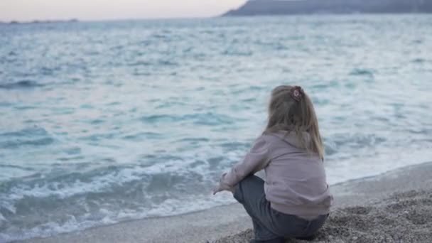 Ein Kind sitzt bei Sonnenuntergang am Meer — Stockvideo