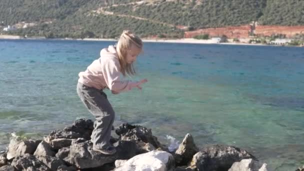 Türkiye 'de ilkbaharda deniz kenarındaki bir kayanın üzerinde duran küçük bir kız çocuğu — Stok video