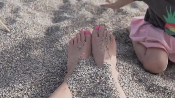 Kinderen begraven hun moeders voeten met zand op een kiezelstrand — Stockvideo