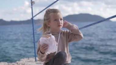 Şirin küçük kız sahilde fast food yiyor.