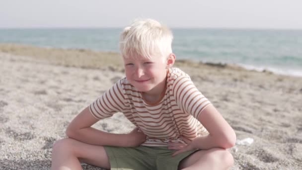 Close-up, bahagia anak laki-laki pirang duduk di pantai oleh laut di Turki — Stok Video
