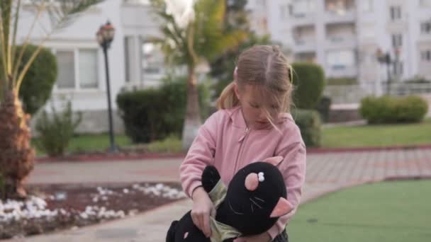 Ένα κορίτσι παίζει με ένα βελούδινο παιχνίδι στην αυλή του σπιτιού την άνοιξη. — Αρχείο Βίντεο