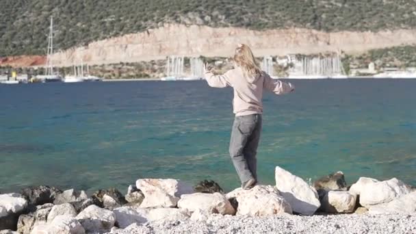 봄철에 한 어린 소녀가 터키의 바위가 많은 해변을 따라 걸어 다닌다 — 비디오