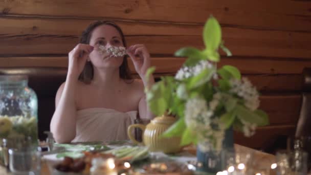Женщина в простыне наслаждается веткой цветущей вишни в ванной за столом — стоковое видео