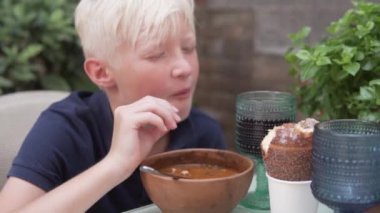 Sarışın bir çocuk caddedeki bir restoranda lezzetli bir çorbanın tadını çıkarıyor..