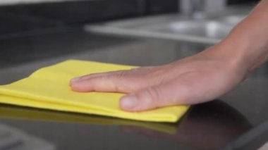 Bir kadın mutfaktaki tezgahı parlak sarı bir bezle siliyor..