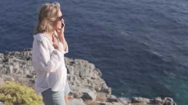 Bir kadın, deniz kıyısındaki bir uçurumda cep telefonuyla konuşuyor. Deniz kenarındaki güzel bir yerden gelen mutlu turist çağrılarını düşünün. Türkiye, Alanya