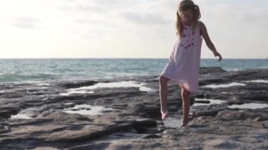 Güzel video, çocuk turizmi konsepti. Küçük bir kız Türkiye 'de vahşi bir Akdeniz plajı boyunca yürüyor.