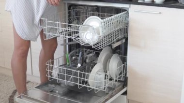 Kadın bir ev hanımı bulaşık makinesine kirli bulaşıkları doldurur..