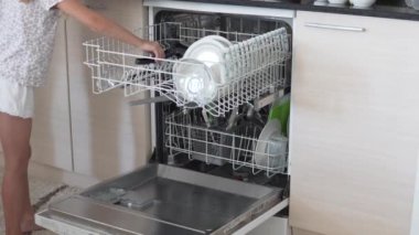 Küçük kızı olan bir anne, sabahları bulaşık makinesine kirli bulaşıkları doldurur..