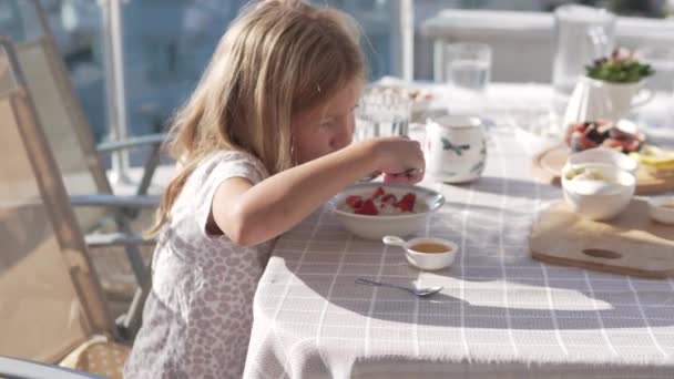 Vacker Liten Flicka Äter Gröt Med Jordgubbar Balkongen Morgonen — Stockvideo