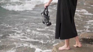 Bir kadın elinde denizin arka planına karşı gaz maskesi tutuyor. Kıyametten sonraki dünya