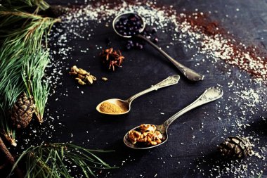 a closeup shot of a bunch of silver spoons herbs and spices on a dark background