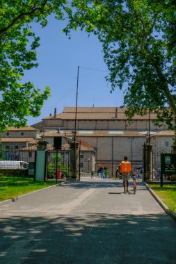 Turuncu sırt çantalı kurye çocuk parktan Palazzo Pilotta 'ya doğru gidiyor.