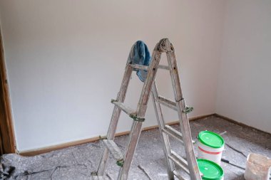 Merdiven, silindir ve boya silindiri. Boya almaya hazır boş bir odada boya kovaları. Duvarları boyamak, yeniden yapılandırma işleri.